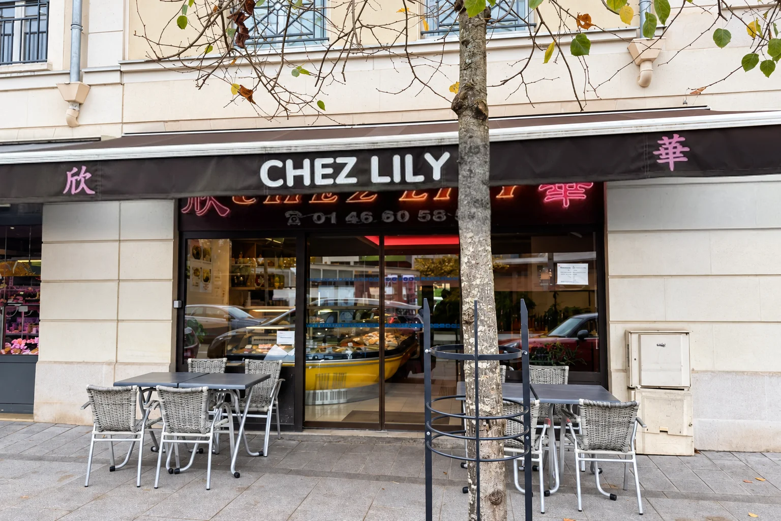 Façade de Chez Lily : store marron, enseigne lumineuse, tables et chaises devant la vitrine